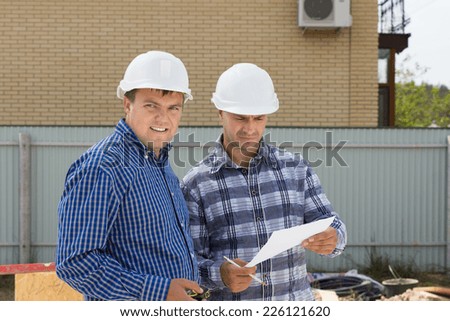 Middle Age Male Building Engineers with White Helmets Visiting Construction Site to Monitor Building Progress.