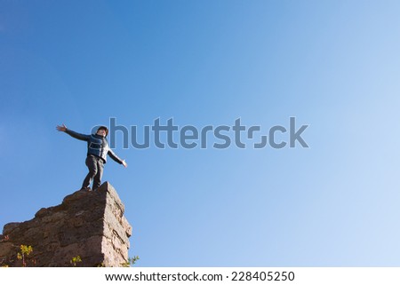Young man celebrating on a ruined building standing on top of a high old stone wall with his arms outspread to the sun against a clear blue sky with lots of copyspace, view from below