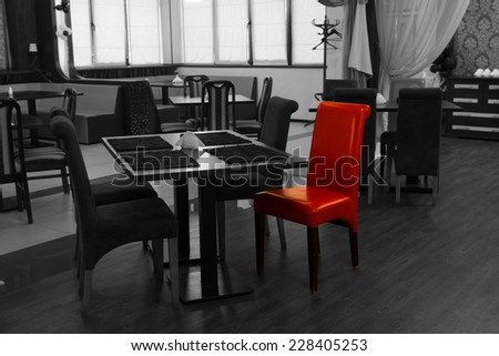 Single red chair in a greyscale nightclub interior with selective color showing modern tables and chairs