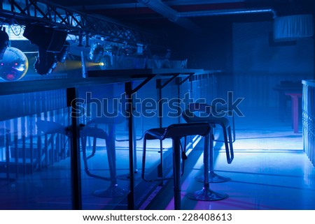 Interior of a modern bar with moody blue lighting and a row of contemporary bar stools in front of a reflective counter in a nightclub