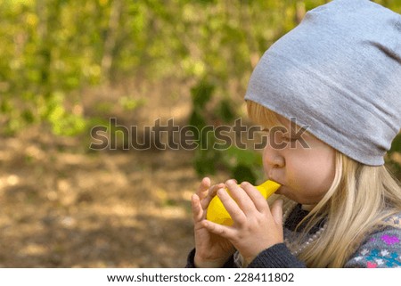 Close up Young Blond Kid in Gray Bonnet Blowing Yellow Balloon Toy for Fun. Outdoor Capture.