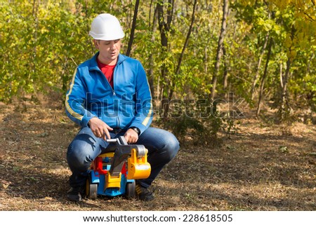 Close up Middle Age Man in Blue Jacket with White Helmet Riding a Truck Toy at the Woodland.
