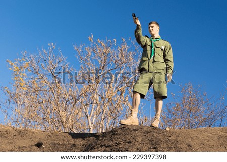 Scout standing on a rock taking a compass reading to get his bearing and location, low angle skyline view