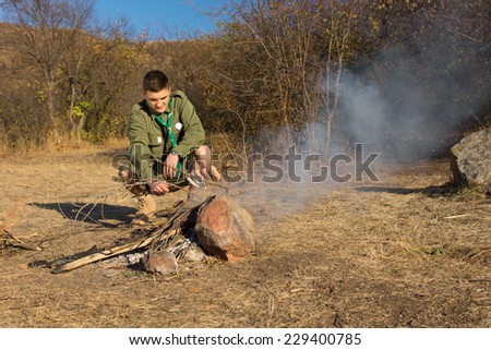 Young Male Scout Grilling Sausages Alone in Old Way at the Grassy Campground.