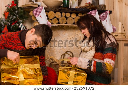 Young couple sitting on the floor in a rustic cabin opening festive gold Christmas gifts with eager anticipation
