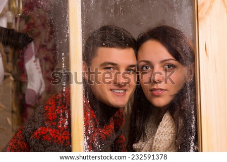 Close up Young Sweet Couple Smiling Behind Glass Window with Touching Faces While Looking at the Camera.