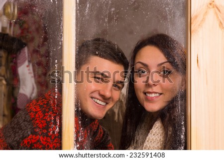 Close up Happy Young Couple in Winter T-Shirts Smiling Behind Glass Windows While Looking at the Camera.