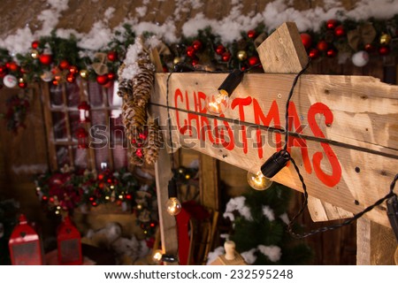 Red Christmas Label on Wooden Booth Wall with Lights and Christmas Ornaments Inside the House.
