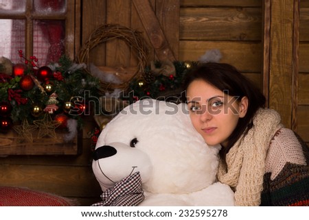 Close up Young Adult Woman in Winter Outfit Hugging White Bear Doll on Wooden Wall Background with Christmas Decorations.