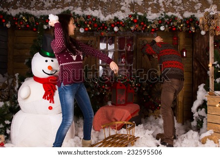 Young Couple Playing with Cotton Snow Inside the Wooden House with Snowman and Various Christmas Decors.