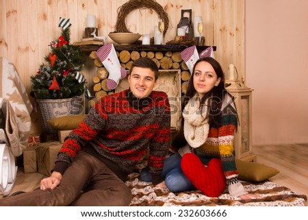 Portrait of Couple Wearing Sweaters Sitting on Floor inside Log Cabin in Winter