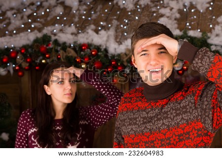 Couple Wearing Sweaters Looking into the Distance Outdoors in Winter in front of Log Cabin