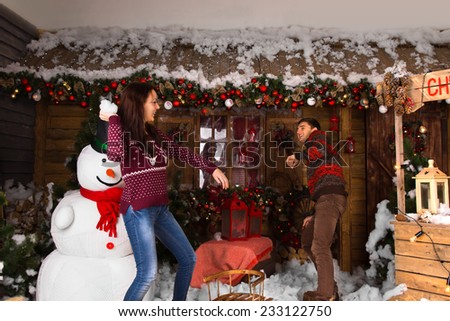 Young Woman Throwing Cotton Snow to her Partner While Playing Inside the Wooden House with Snowman and Assorted Beautiful Christmas Decorations.