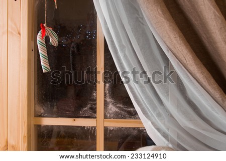 Christmas candy cane hanging in a rustic wooden window with winter frost and the drape pulled back against the darkness outside