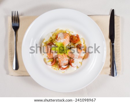 Gourmet salmon seafood starter with bite sized portions of fish drizzled with a cream sauce and seasoned with herbs, overhead view on a white plate