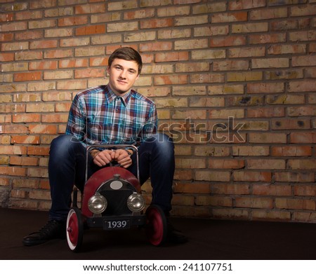 Good Looking Young Man in Checkered Shirt and Jeans Playing with Toy Automobile With Brick Wall Background.