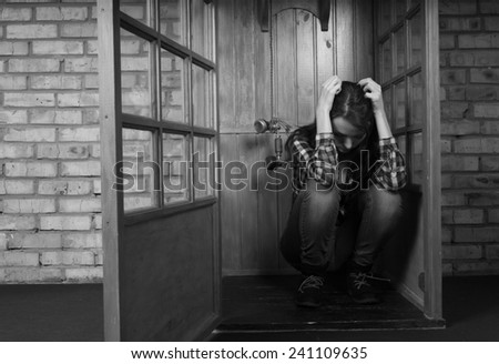 Troubled Woman Holding Head in Hands and Crouching in Public Telephone Booth