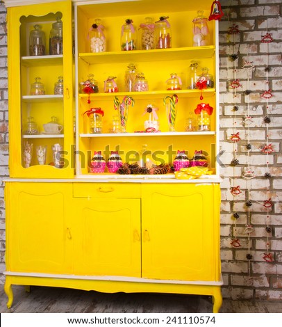 Colorful bright yellow welsh dresser with its shelves filled with decorative glass jars of kitchen ingredients and decorated with striped candy canes and ribbon