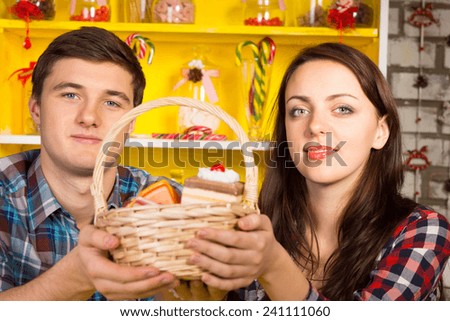 Smiling couple holding up a wicker basket of replica cookies and cakes with a colorful yellow Welsh dresser with glass jars and candy canes in the background