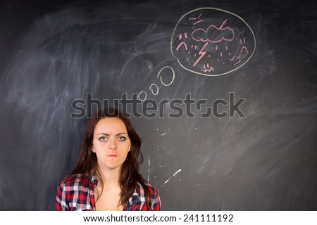 Angry young woman glaring at the camera in a depiction of rage as shown by the hand-drawn diagram of a bolt of lightning and thunder on the chalkboard alongside her