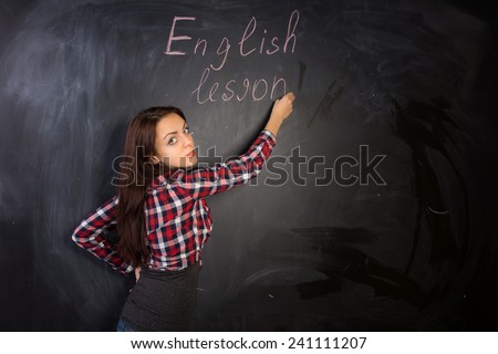 Attractive female teacher giving an English lesson writing on the class black board and turning back with a serious expression towards the camera