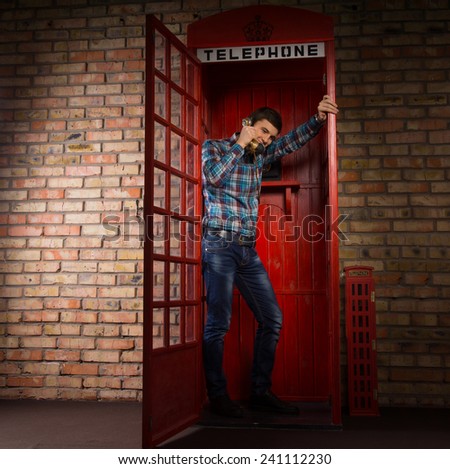 Man standing chatting in a replica red British phone booth standing leaning against the open door, full length view
