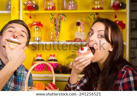 Young Couple Doing Eating a Cake Pose at the Cafe While looking at the Camera. Captured with Candy Jars Display at the Back.