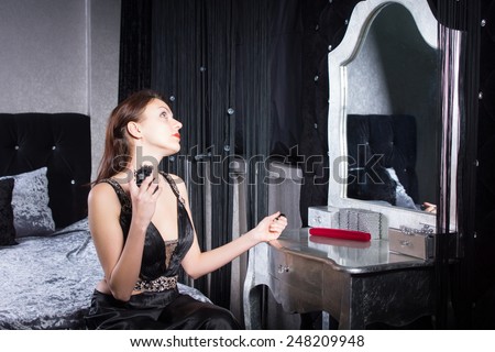 Elegant young woman applying perfume as she sits in front of the mirror at her dressing table in a stylish grey and white bedroom