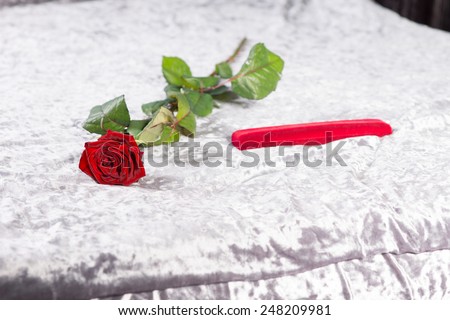 Special romantic Valentines gift of a single long-stemmed red rose and gift-wrapped red present lying on the bed on the white bedspread