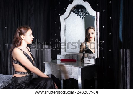 Seated Pretty Woman in Elegant Black Dress in Front a Mirror Inside her Room.