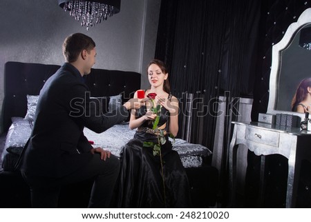 Kneeling Young Man Offering a Jewelry Gift to his Happy Pretty Girlfriend While at the Bedroom.