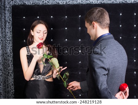 Young man proposing to his sweetheart first offering her a single long-stemmed red rose before producing the ring from behind his back