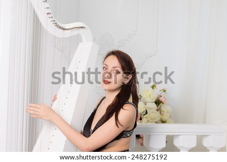 Pretty elegant female musician in black evening wear sitting playing the harp running her fingers over the strings as she looks at the camera