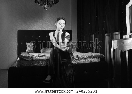 Pretty Young Woman in Dress Holding Rose Flower While Sitting at the Bedroom. Captured in Monochrome.