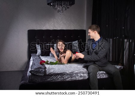 Young Man Surprises his Girlfriend Lying on Bed with Ring Jewelry in a Red Box