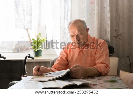 Close up Old Bald Man Reading News Updates on Tabloid While Sitting at the Living Room Near the Window.