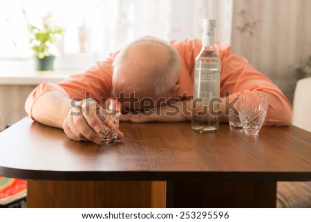 Close up Drunk Old Bald Man Leaning on the Wooden Table with Vodka Holding a Small Glass
