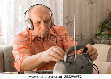 Close up Old Man Listening News Program at the Radio with Headset While Sitting at the Living Area.