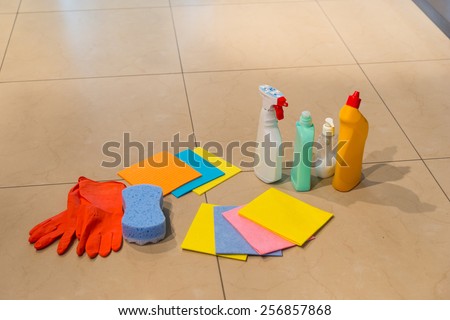 Various colorful household cleaning supplies displayed on a floor with rubber gloves, clothes, a sponge and spray bottles and containers, with copyspace