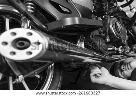 Young Guy Lying on the Floor Repairing his Sports Motorbike Using Hand Tool in Monochrome Color.