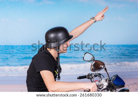 Young man in a helmet saluting as he rides a motorbike along the seashore on a hot sunny summer day