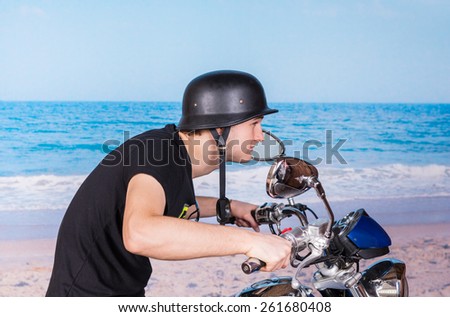 Young man in a retro helmet speeding on his motorbike as he crouches low over the handlebars while riding alongside the sea