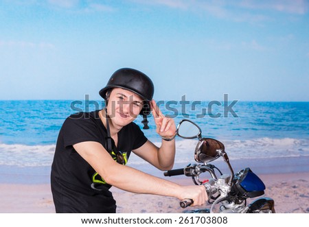 Handsome young man wearing an old-fashioned helmet saluting on his motorbike as he spends a relaxing day at the seaside