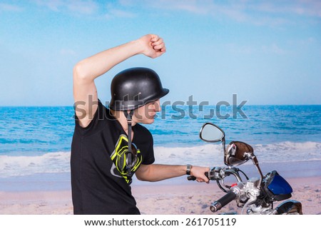 Young Handsome Man Riding a Motorbike at the Beach with One Arm Raised on a Blue Tranquil Ocean Background.