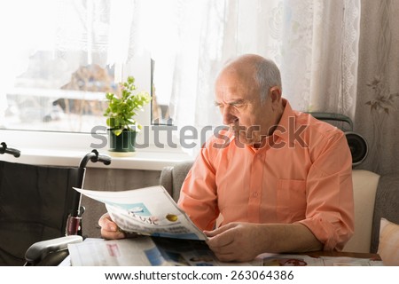 Close up Sitting Pensioner Reading News on Tabloid While Resting at the Living Area Near the Window.