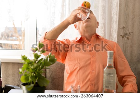 Close up Playful Elderly Drinking Vodka Wine with Apple on Forehead While Sitting at the Living Area Close to the Window.
