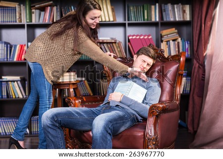 Librarian trying to wake a sleeping man who has dozed off in an armchair in the library tapping him on the cheek