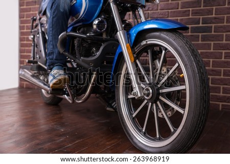 Man Riding a Blue Sports Motorbike on the House Wooden Floor, Emphasizing the Wheel in Close up.