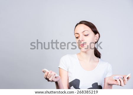 Close up Undecided Young Woman Holding Two Foundation Make ups, Thinking which one to use, on a White Background.