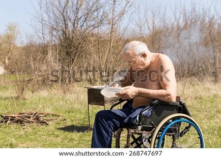 Disabled Old Man with No Shirt Sitting on his Wheelchair and Eating his Lunch at the Park Alone on a Very Sunny Day.